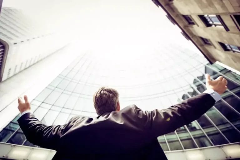 A businessman with his arms outstretched in front of a skyscraper.